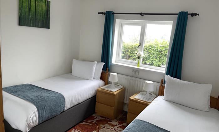 Twin bedroom with 2 full size single beds, 2 bedside cabinets, mirror wardrobe and window overlooking the private garden area